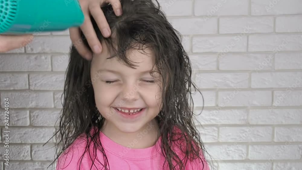 Mother drying childs hair. Portrait of adorable little girl while drying her hair with a hairdryer.