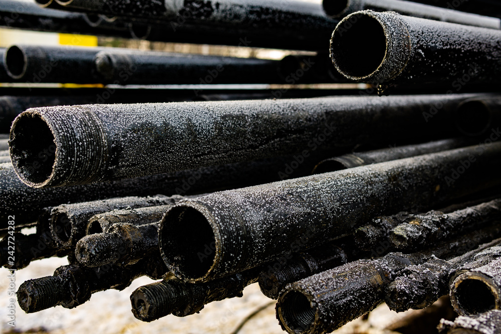Oil Drill pipe. Rusty drill pipes were drilled in the well section. Downhole drilling rig. Laying the pipe on the deck. View of the shell of drill pipes laid in courtyard of the oil and gas warehouse. Oil Drill pipe. Rusty drill pipes were drilled in the well section. Downhole drilling rig. Laying the pipe on the deck. View of the shell of drill pipes laid in courtyard of the oil and gas warehouse.
