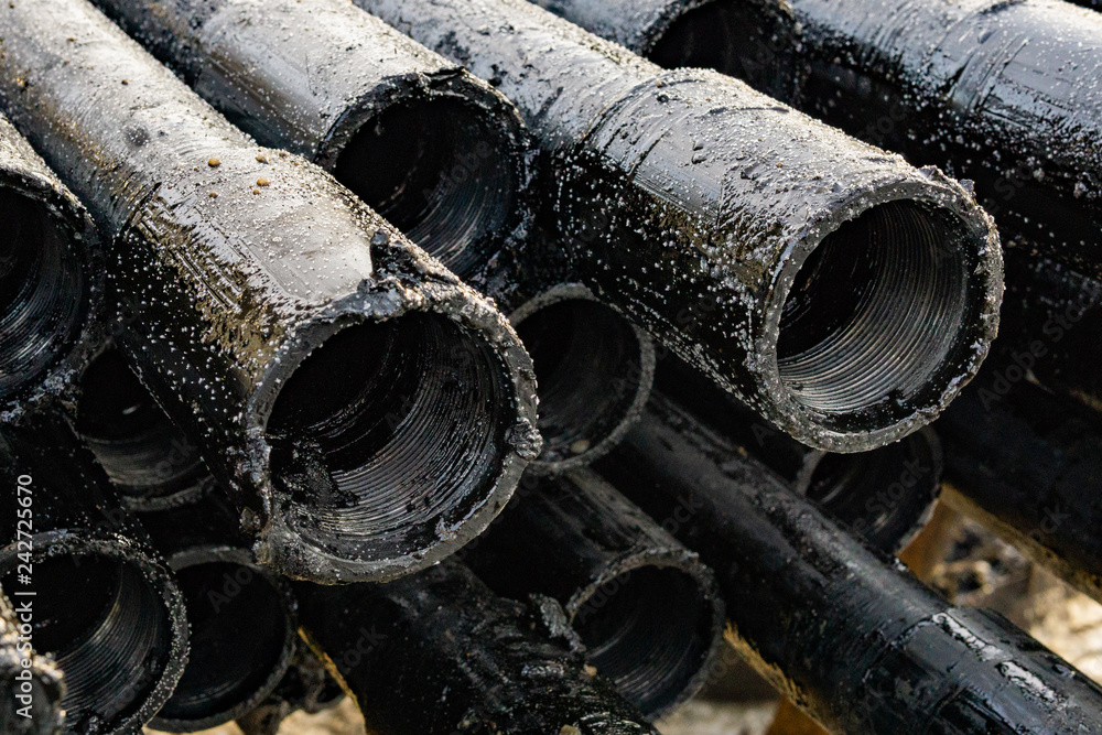 Oil Drill pipe. Rusty drill pipes were drilled in the well section. Downhole drilling rig. Laying the pipe on the deck. View of the shell of drill pipes laid in courtyard of the oil and gas warehouse. Oil Drill pipe. Rusty drill pipes were drilled in the well section. Downhole drilling rig. Laying the pipe on the deck. View of the shell of drill pipes laid in courtyard of the oil and gas warehouse.