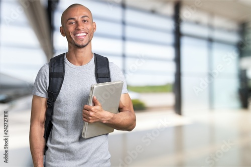 Smiling African Student man with laptop, mall background, bokeh