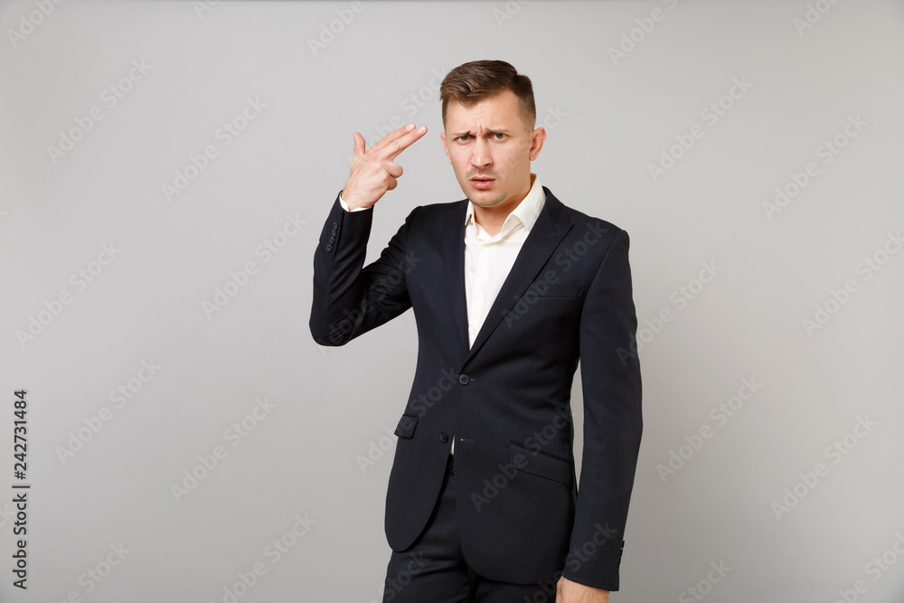 Puzzled young business man in classic black suit, shirt point fingers to head as if he about shoot himself isolated on grey background. Achievement career wealth business concept. Mock up copy space. Puzzled young business man in classic black suit, shirt point fingers to head as if he about shoot himself isolated on grey background. Achievement career wealth business concept. Mock up copy space.