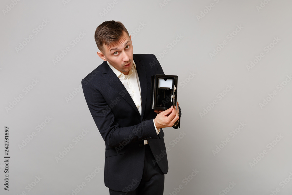 Curious young business man in classic black suit white shirt opening metal bank safe for money accumulation isolated on grey background. Achievement career wealth business concept. Mock up copy space. Curious young business man in classic black suit white shirt opening metal bank safe for money accumulation isolated on grey background. Achievement career wealth business concept. Mock up copy space.
