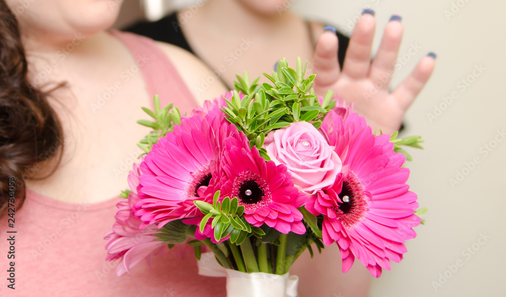 A beautiful bridesmaid holding a bouquet of warm pink beautiful organic natural flowers into the camera with a shallow depth of field. conceptual image for a wedding celebration.