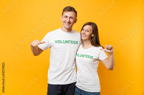 Fotografie Portrait of young colleagues couple in white t-shirt with written inscription green title volunteer isolated on yellow background