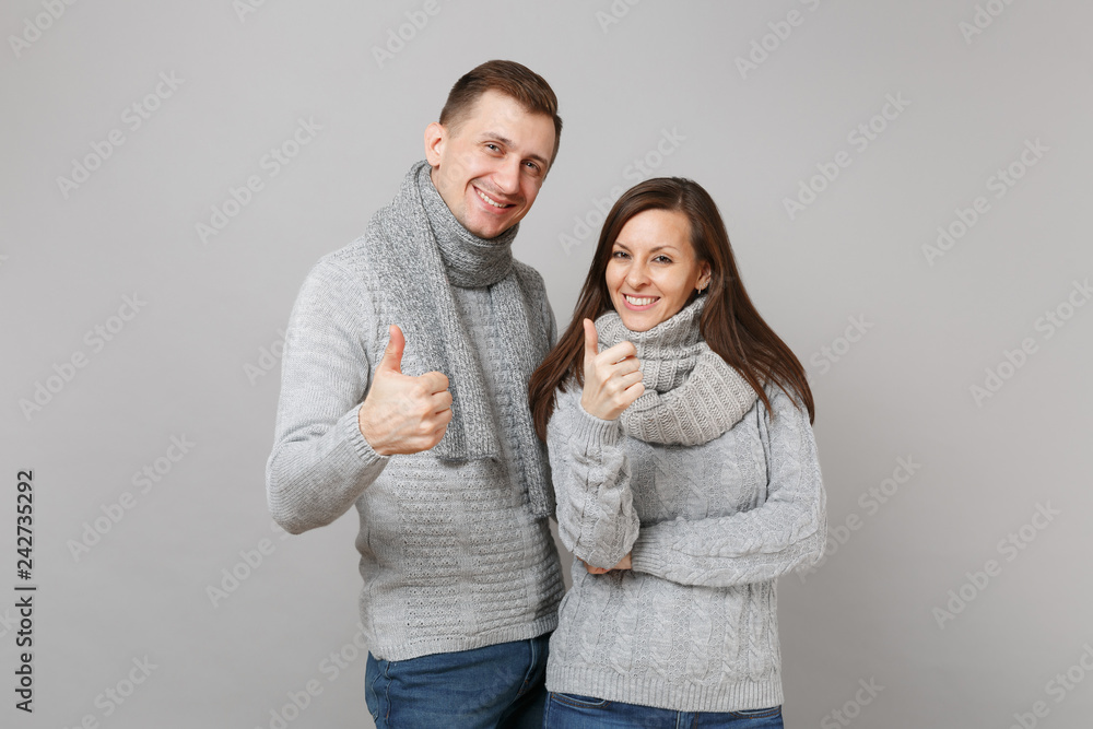 Young cute couple girl guy in gray sweaters, scarves together isolated on grey wall background, studio portrait. Healthy lifestyle, ill sick disease treatment, cold season concept. Mock up copy space. Young cute couple girl guy in gray sweaters, scarves together isolated on grey wall background, studio portrait. Healthy lifestyle, ill sick disease treatment, cold season concept. Mock up copy space.