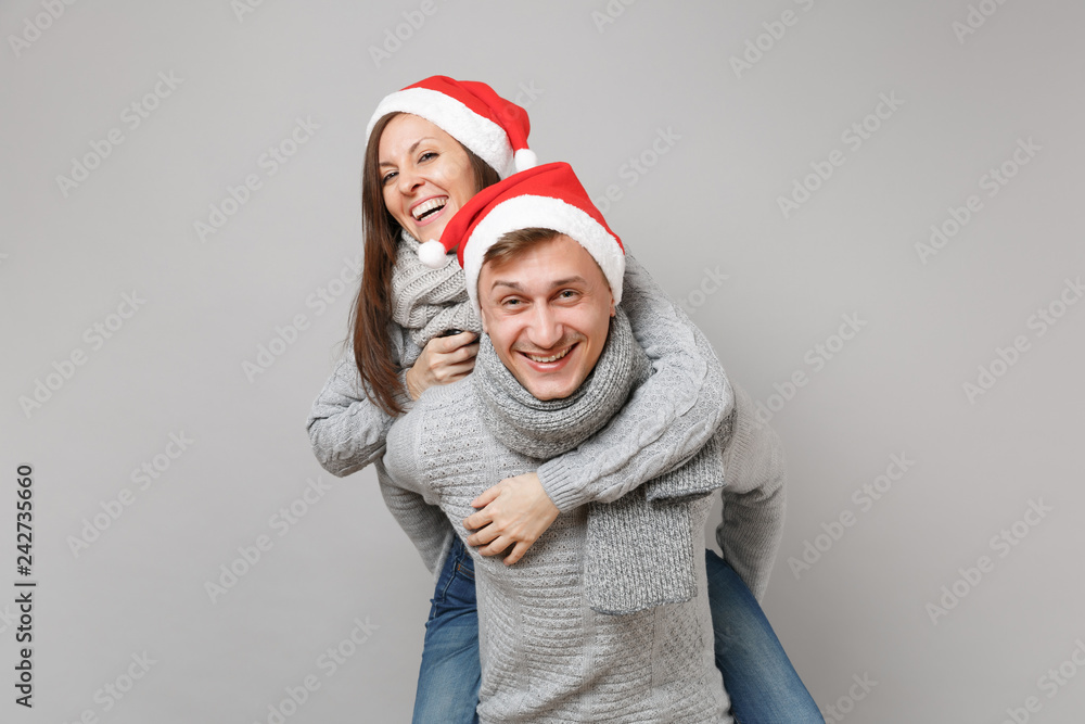 Merry fun couple girl guy in red Santa Christmas hat gray sweaters scarves isolated on grey wall background, studio portrait. Happy New Year 2019 celebration holiday party concept. Mock up copy space. Merry fun couple girl guy in red Santa Christmas hat gray sweaters scarves isolated on grey wall background, studio portrait. Happy New Year 2019 celebration holiday party concept. Mock up copy space.