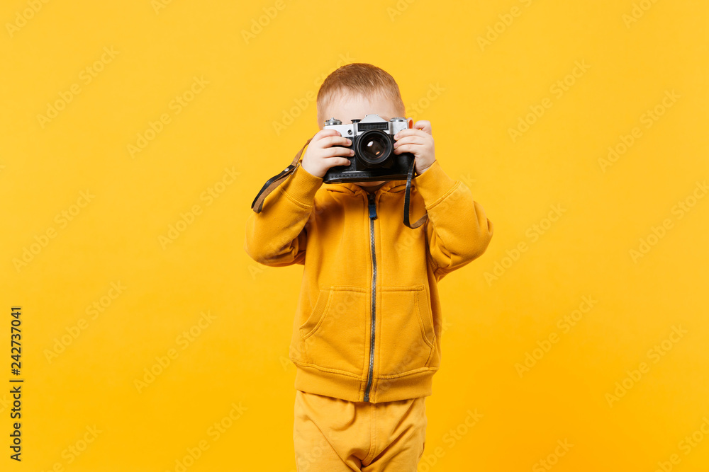 Little kid boy 3-4 years old wearing yellow clothes hold camera isolated on orange wall background, children studio portrait. People sincere emotions, childhood lifestyle concept. Mock up copy space. Little kid boy 3-4 years old wearing yellow clothes hold camera isolated on orange wall background, children studio portrait. People sincere emotions, childhood lifestyle concept. Mock up copy space.