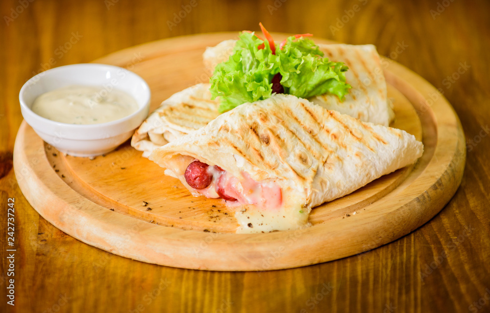 Lavash burrito stuffed meat sausage and cheese sauce served salad. Meat wrapped with lavash burrito. Restaurant meal traditional cuisine. Burrito tortilla served wooden board. Restaurant food concept