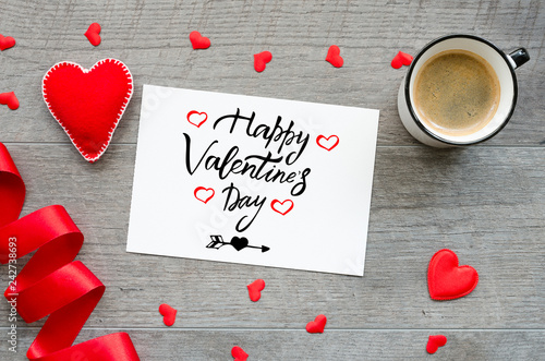 Handwritten greeting card with text Happy Valentines day on wooden background with red hearts, ribbon and coffee cup