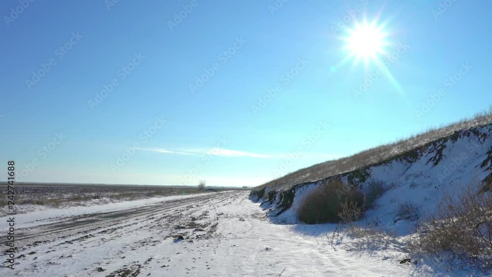 Thaw, melting snow in the field. Dry grass makes its way through the snow cover. Country road in a winter field. The end of winter. Thaw, melting snow in the field. Dry grass makes its way through the snow cover. Country road in a winter field. The end of winter.