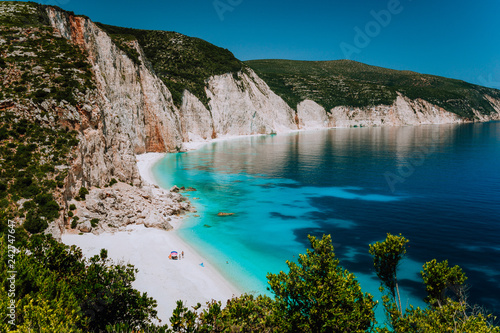Amazing Fteri beach lagoon, Kefalonia, Greece. Tourists under umbrella chill relax near clear blue emerald turquoise sea water