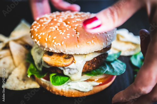 Burger Woman hand with red nails picking up and holding delicious snack food on background blurred