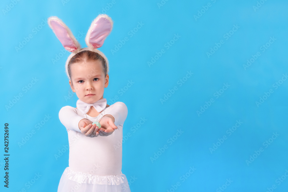 A child wearing a white rabbit. A little girl stretches an Easter egg in her hands. Cute bunny, holiday symbol. Bright photo on a blue background.