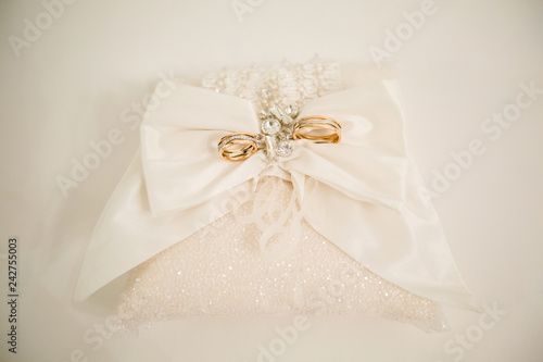 A pair of wedding rings on a white pillow, the top of which is made in the shape of a butterfly. Between the rings there are several decorations. Photo close up.