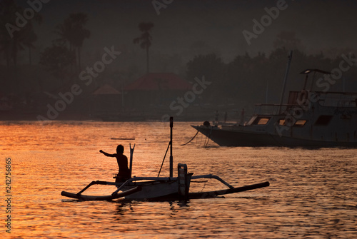 Fisherman Paddling a Small Outrigger in the Village of Pemuteran, Bali, Indonesia. At dawn a fisherman hopes the reef will provide a catch of mackerel to feed his family and provide a small income. photo
