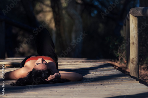 Mujer joven morena en primer plano tumbada en el camino del bosque