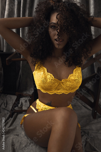 curly brunette in yellow lingerie looks into the camera sticking her tongue out