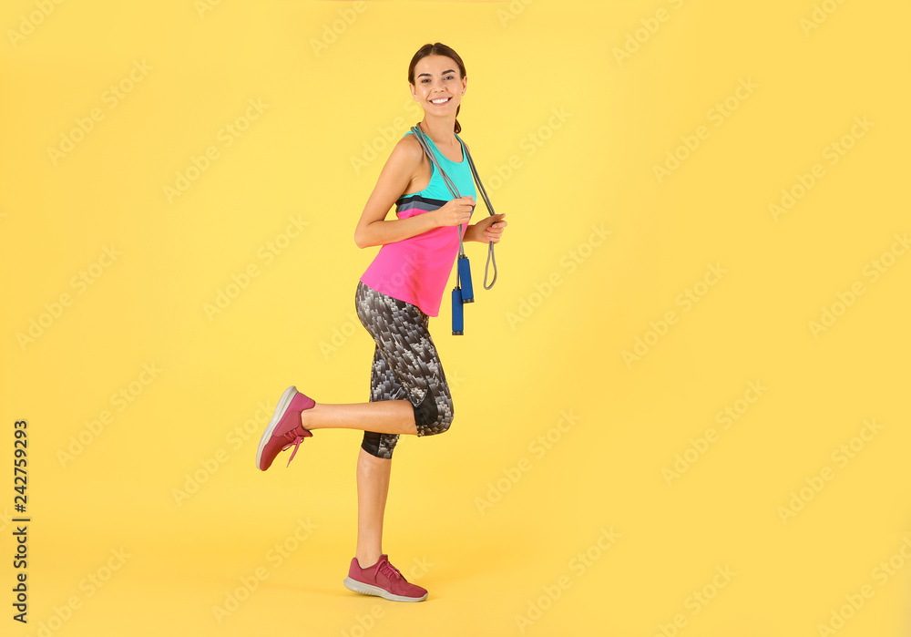 Full length portrait of young sportive woman with jump rope on color background