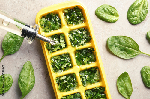 Pouring oil into ice cube tray with spinach on grey background, top view
