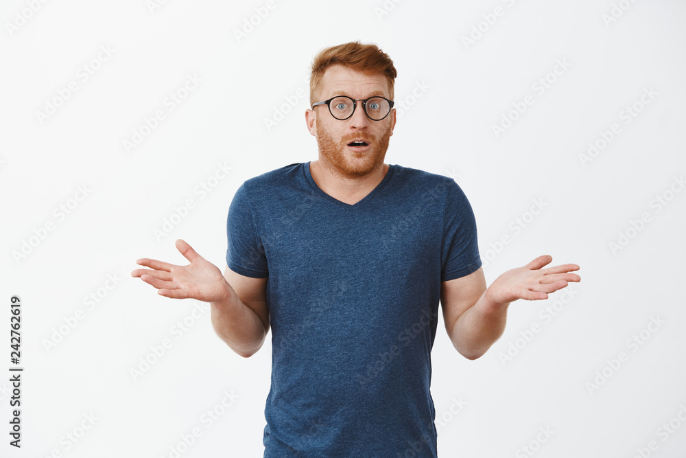 I have no idea how that happened. Portrait of clueless cute masculine male with red hair in glasses and t-shirt, shrugging with spread palms and gazing confused and uncertain at camera over grey wall I have no idea how that happened. Portrait of clueless cute masculine male with red hair in glasses and t-shirt, shrugging with spread palms and gazing confused and uncertain at camera over grey wall