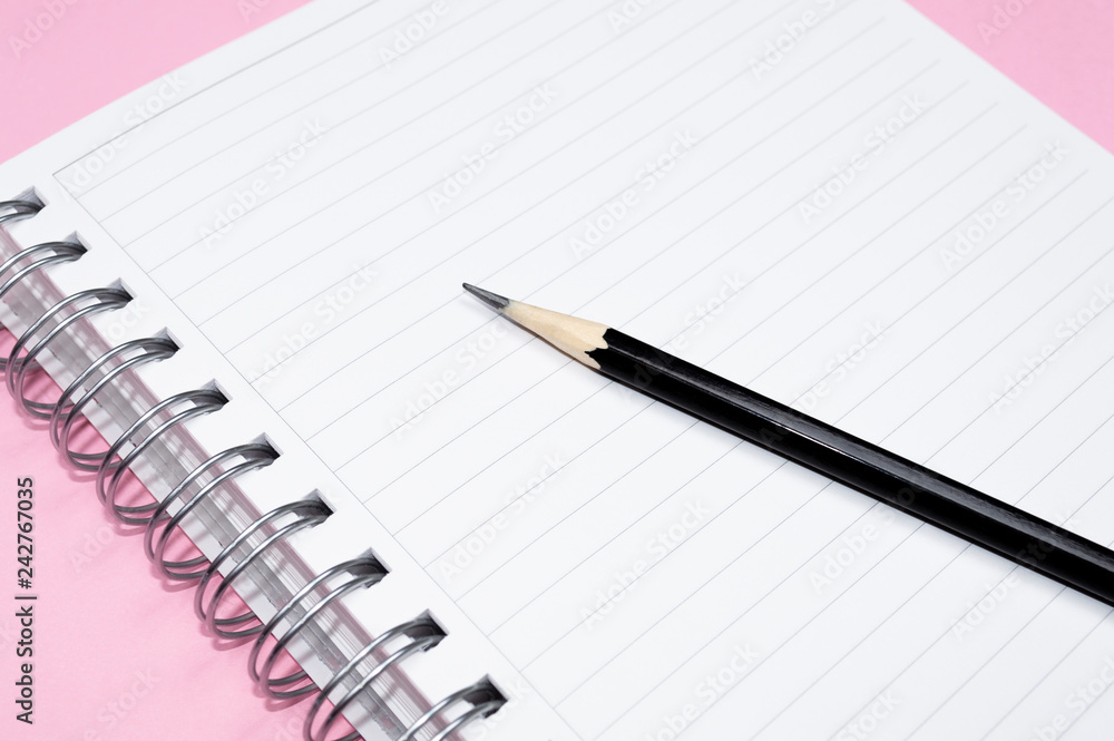 Working space: notepad and black pencil on pink background. Minimalist composition. Working space: notepad and black pencil on pink background. Minimalist composition.