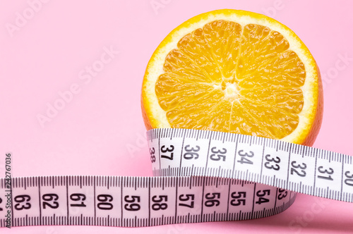 Sliced orange and measuring tape on pink background. Diet concept.