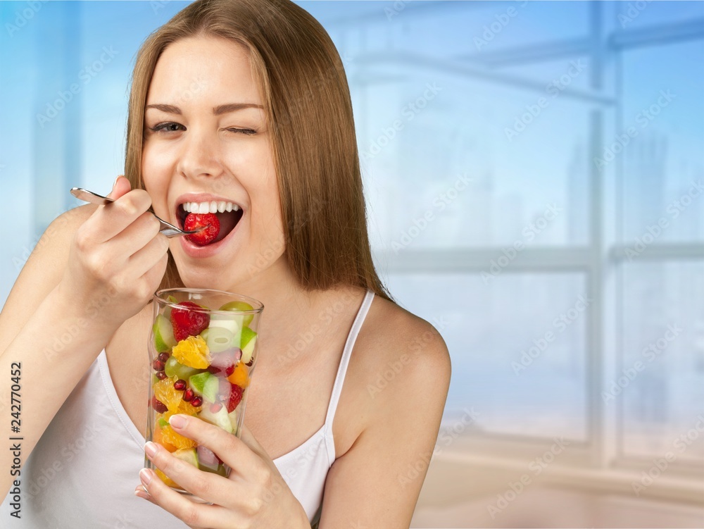 Young woman eating fruits from glass on blurred background Young woman eating fruits from glass on blurred background