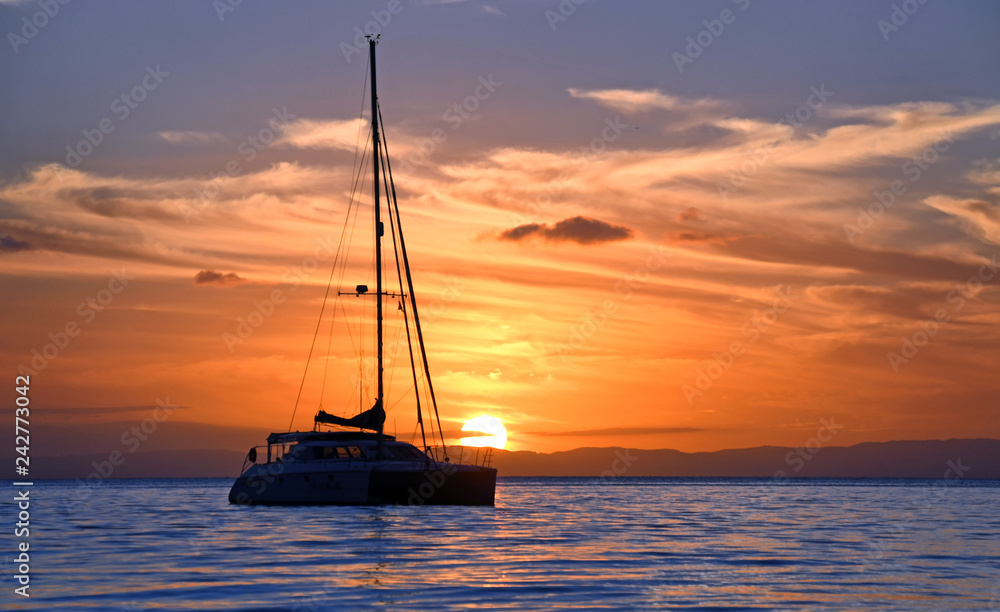 Yacht sits in tranquil bay at sunset.
