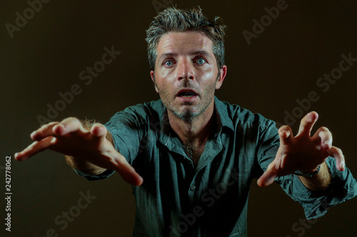 hypnotized and mesmerized facial expression portrait of young attractive and dazed man raising hands zombie like raising hands and eyes wide opened isolated on black photo