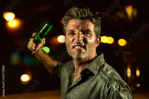 Foto young upset and aggressive drunk man in pub at night holding beer bottle threate