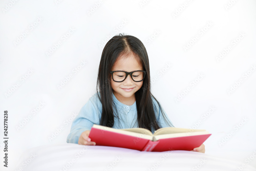 Beautiful happy little Asian kid girl reading hardcover book lying on bed against white background. Beautiful happy little Asian kid girl reading hardcover book lying on bed against white background.