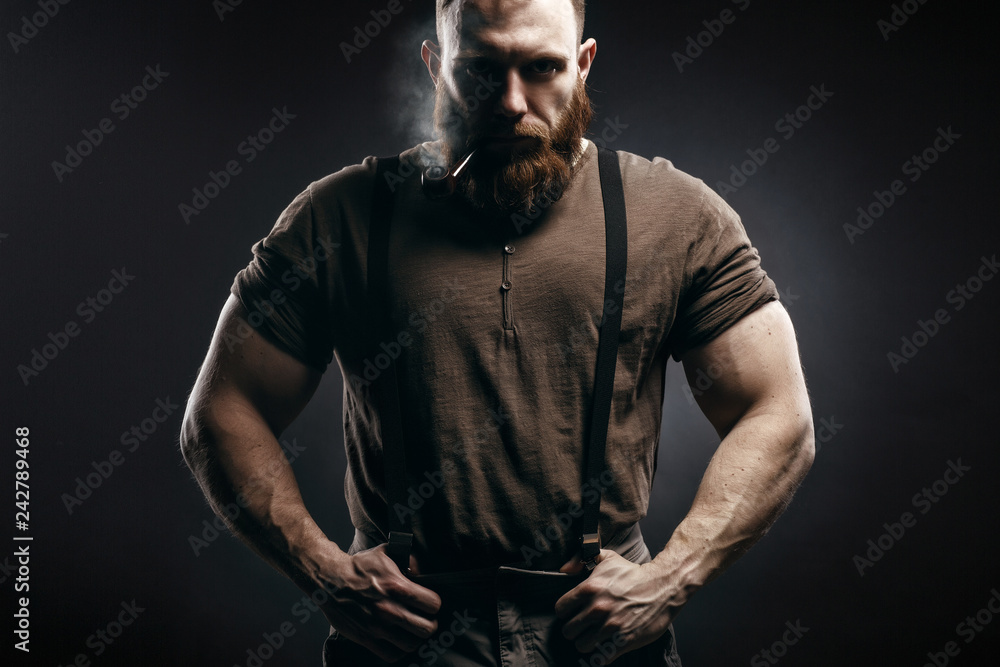 Lumberjack brutal red beard muscled man in brown shirt with smoking tube  standing on dark background Photos | Adobe Stock