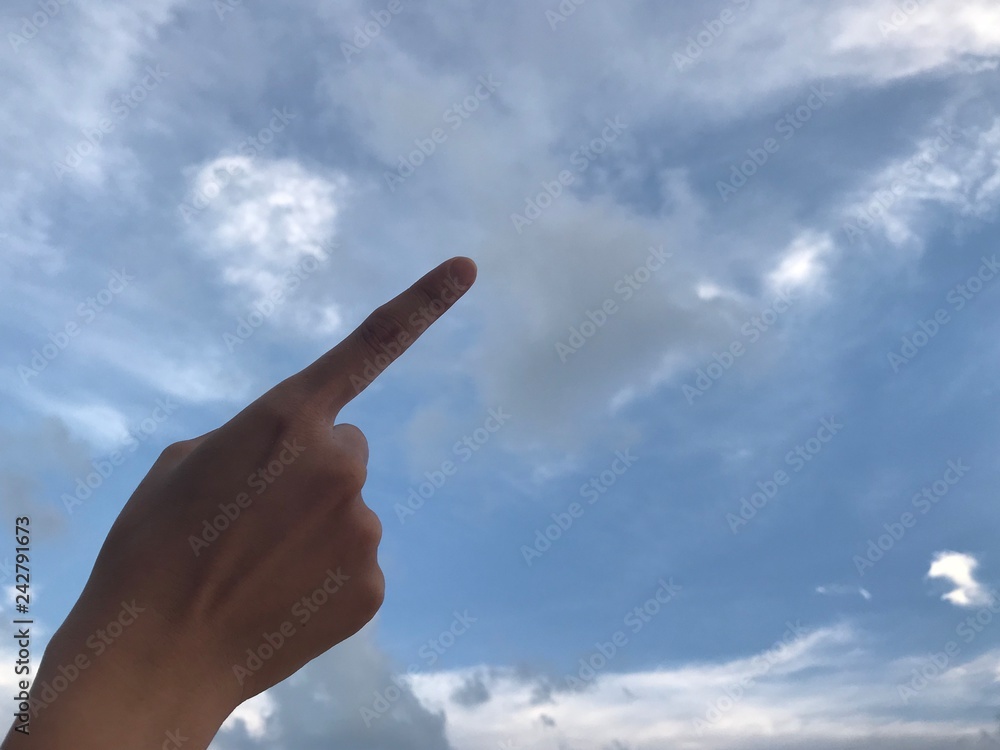 woman use her right index finger pointing up in the bright blue sky with white cloud in daylight with copy space on the right side of frame woman use her right index finger pointing up in the bright blue sky with white cloud in daylight with copy space on the right side of frame