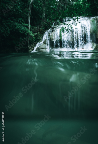 A waterfall taken from below the water with a fish in the foreground and the waterfall in the background within a beautiful jungle in Thailand in Asia in a healthy natural environment