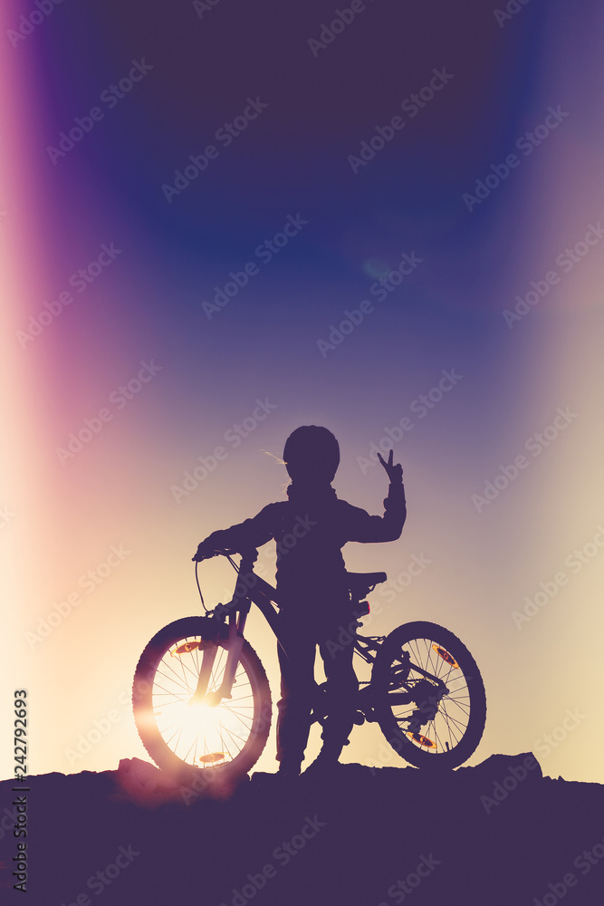 Fototapeta premium Silhouette of a little girl with a bicycle at sunset