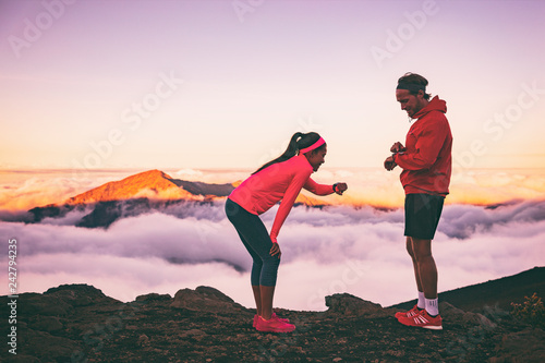 Runners tired exhausted during cardio effort using their wearable technology smartwatch checking heart rate monitor. Two athletes couple running together in outdoors mountains landscape.
