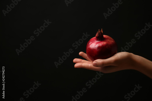 Female hand with ripe pomegranate on dark background