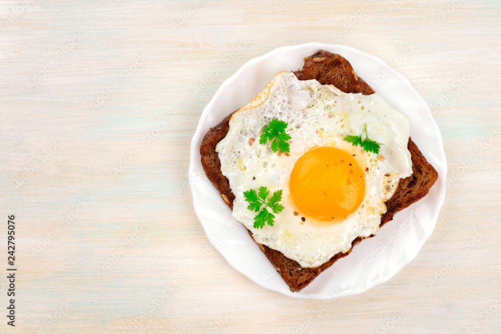 A sunny side up fried egg on a bread toast, shot from above on a pale wooden background with a place for text A sunny side up fried egg on a bread toast, shot from above on a pale wooden background with a place for text