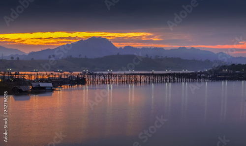 sunrise at Sangkhlaburi, river view morning on the river of old wooden bridge (Mon Bridge) with reflection on the water, mountain and colorful of yellow sun light in the sky,  Kanchanaburi, Thailand. © Yuttana Joe