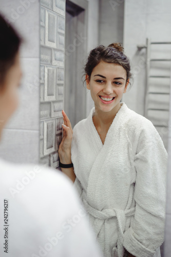 portrait of a beautiful woman in the bathroom. cheerful young girl looks at herself in the mirror, grimaces