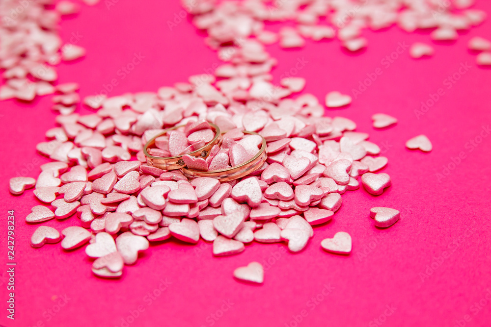 Love and marriage concept. Valentine's Day. Two golden wedding rings lying among lots of light pink small hearts on pink background