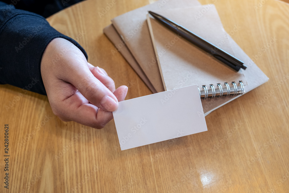 A woman holding and giving a blank empty business card to someone with notebooks on wooden table A woman holding and giving a blank empty business card to someone with notebooks on wooden table