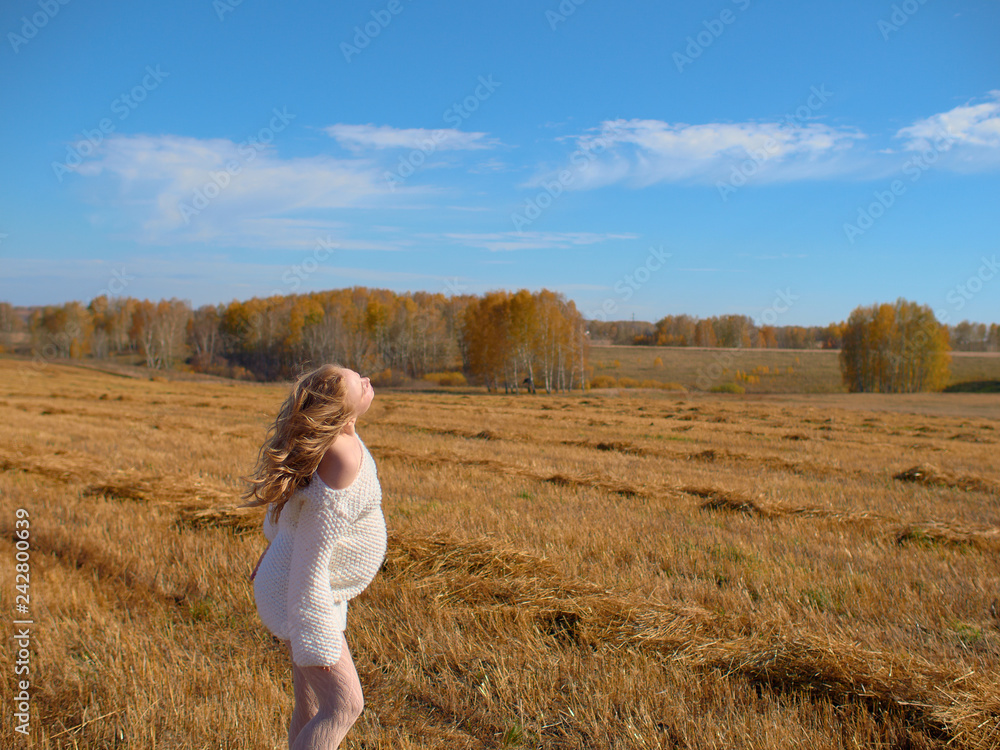 Beautiful pregnant woman in a white woolen sweater. Happy pregnant woman posing on a mown wheat field. Beautiful pregnant woman in a white woolen sweater. Happy pregnant woman posing on a mown wheat field.