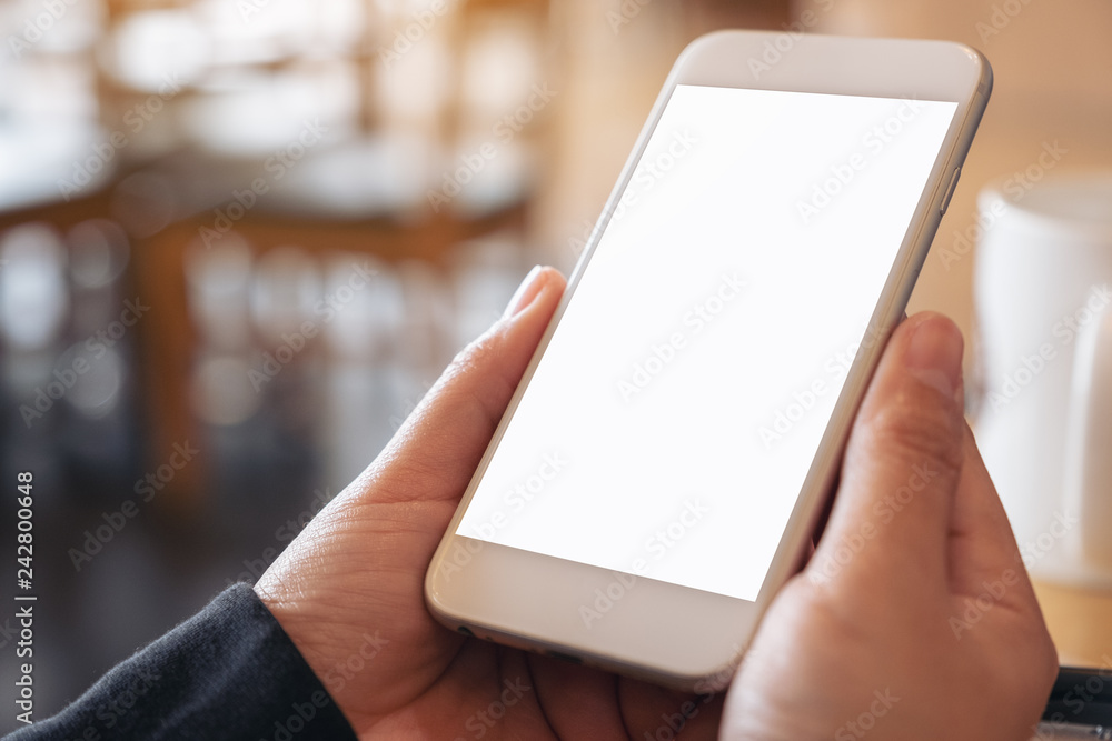 Mockup image of hands holding and using a white mobile phone with blank screen in cafe Mockup image of hands holding and using a white mobile phone with blank screen in cafe