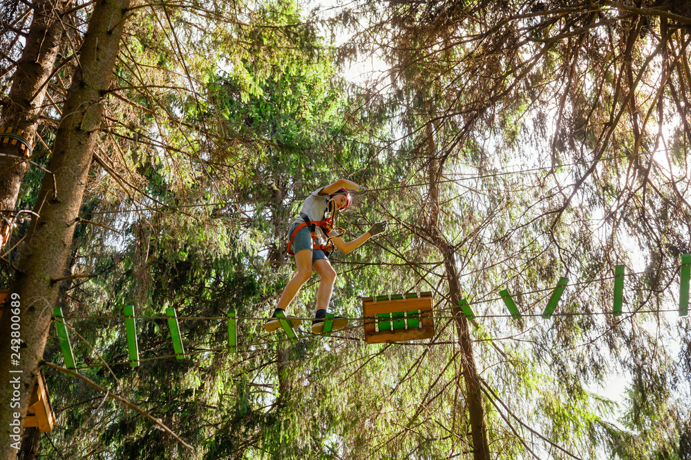 Teen boy on a ropes course in a treetop adventure park passing hanging rope obstacle Teen boy on a ropes course in a treetop adventure park passing hanging rope obstacle
