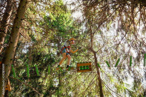 Teen boy on a ropes course in a treetop adventure park passing hanging rope obstacle