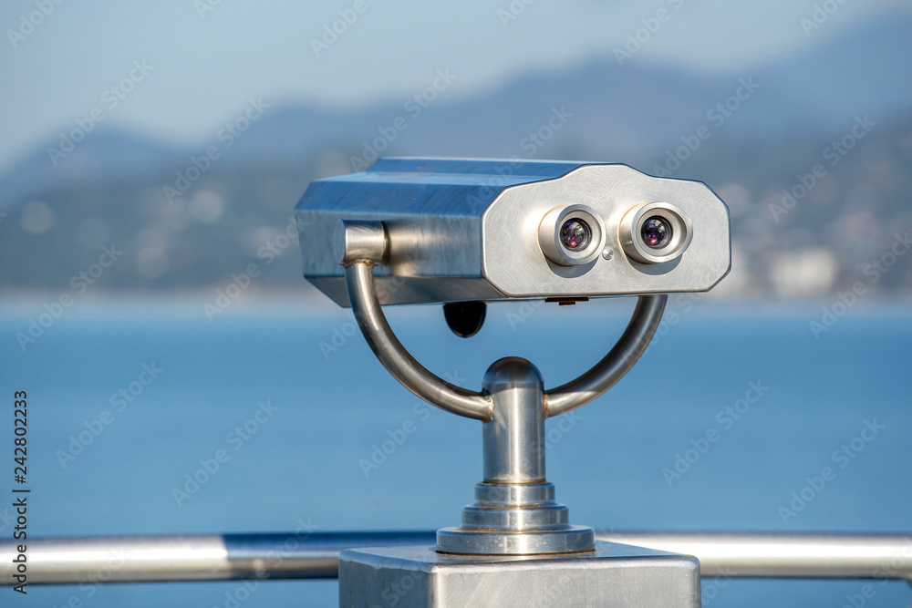 Public binocular on sea shore, close up. Coin operated binocular viewer on blurred background of sunset and sea