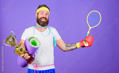 Choose favorite sport. Sport concept. On way to achievement. Man bearded athlete hold sport equipment jump rope fitness mat boxing glove expander racket and golden goblet. Sport shop assortment © be free