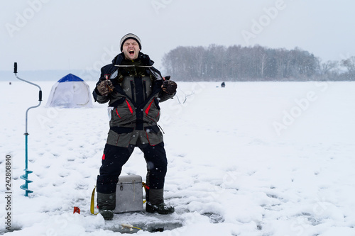 Happy shouting adult fisherman after successful winter fishing at cold winter day