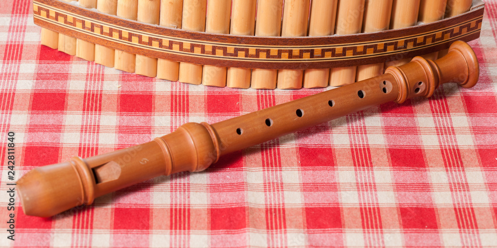 Une flûte à bec et une flûte de Pan posées sur une nappe à carreaux